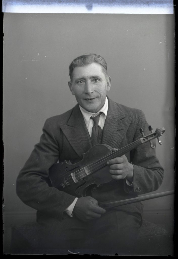 Mustavalkoinen valokuva miehestä, jolla on sylissä viulu.