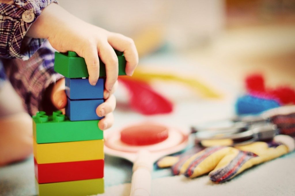 Valokuvas, jossa lapsen käsi rakentaa legopalikoita.