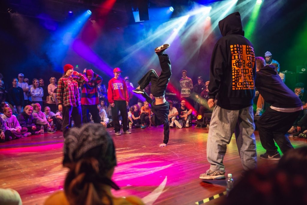 Valokuva breakdance battlesta. Keskellä yksi tanssija ja hänen ympärillään muita ihmisiä.