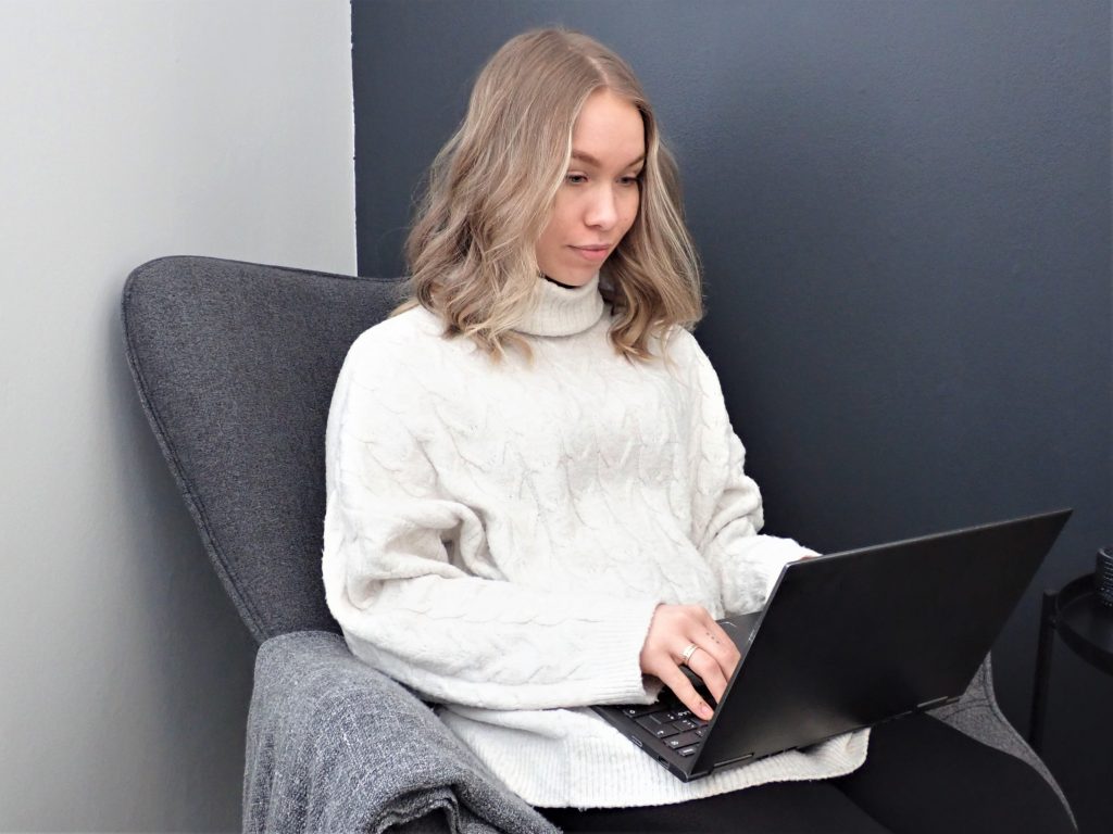 Valokuvassa nainen istuu sohvalla kannettava tietokone sylissä.