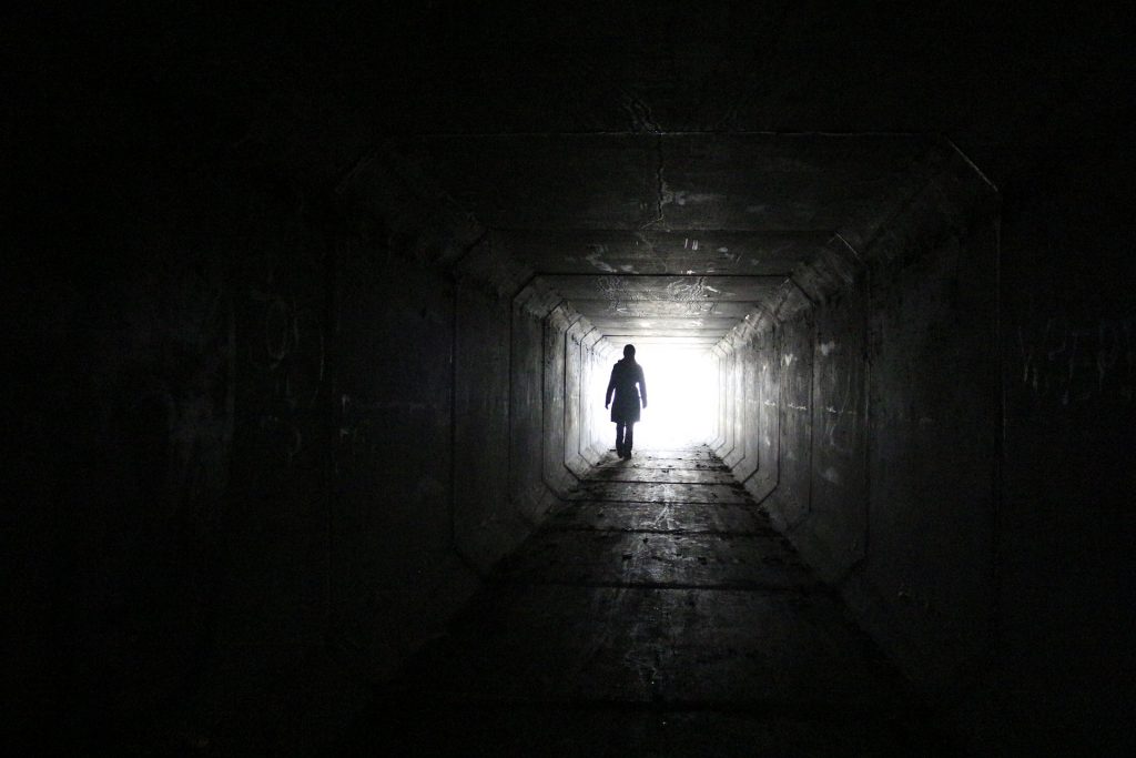 Valokuvassa ihminen pimeässä tunnelissa. Tunnelin päästä näkyy valoa.