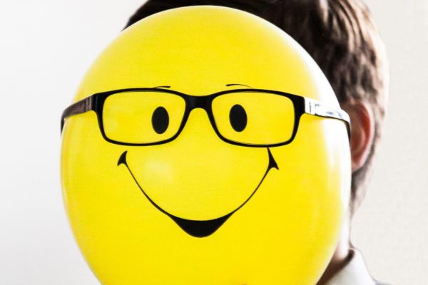 Valokuva, jossa ihmisen pään edessä pidetään keltaista ilmapalloa, jossa hymynaama.