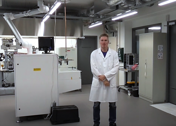 Valokuvassa mies valkoisessa takissa seisoo laboratoriossa.
