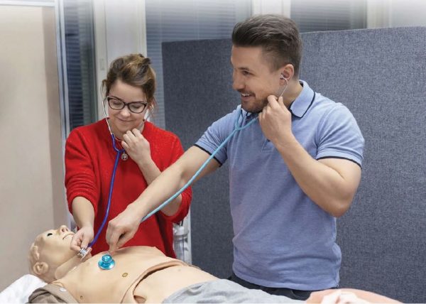 Valokuvassa simulaatiotilanne, jossa kaksi ihmistä kuuntelee potilaan keuhkoja.
