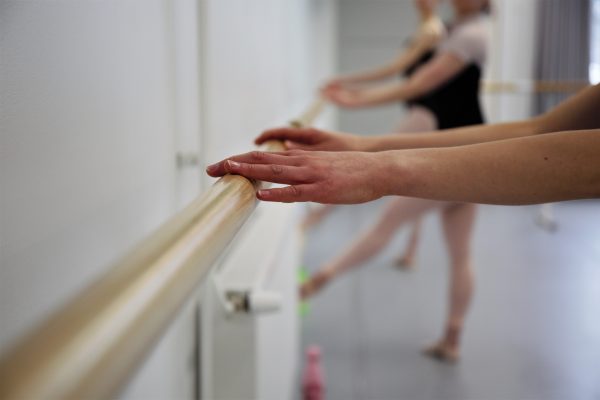 Valokuva, jossa tanssijan käsi ja taustalla balettitanssijoita.