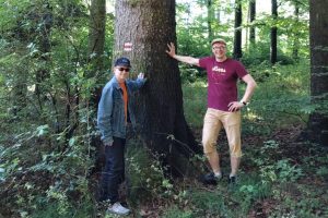 Valokuva, jossa kaksi miestä seisoo suuren puun juurella.
