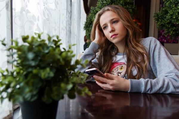 Valokuvassa tyttö istuu älypuhelin kädessään.