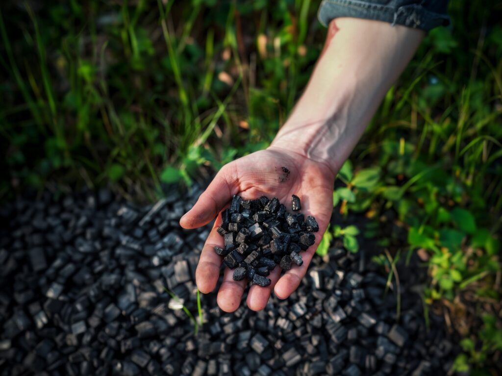 Käsi maastossa pitelemässä biohiiltä