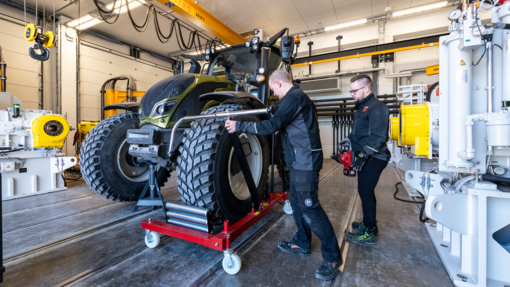 Kaksi miestä mustissa vaatteissa korjaa traktoria laboratoriossa.